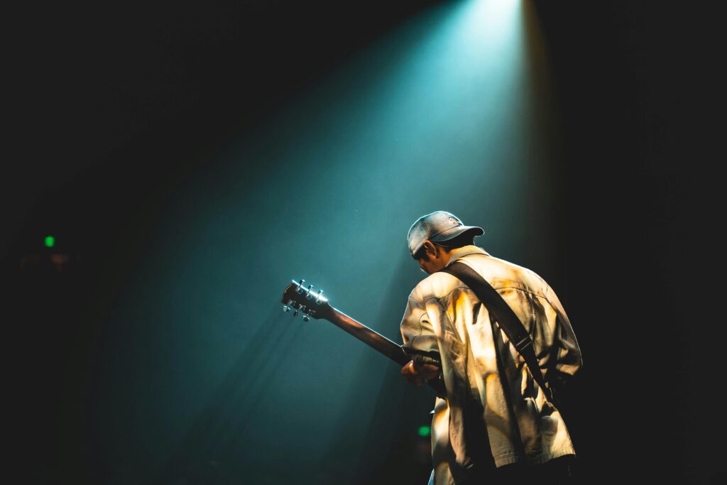 A musician performing live on stage under dramatic lighting, playing a guitar.